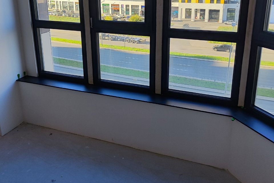 Эркерный подоконник из HPL компакт пластика черного цвета, установленный в панорамном окне с видом на современные высотные здания.