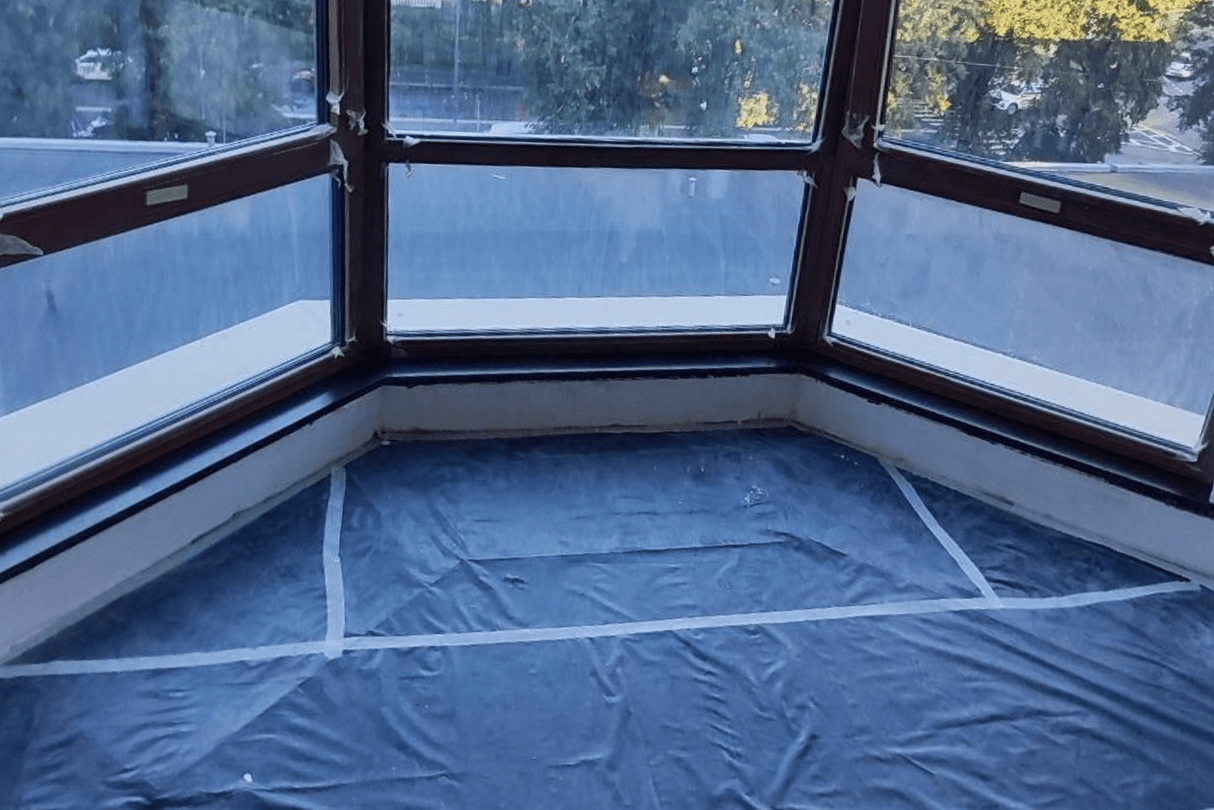 Чёрный эркерный подоконник из акрилового камня с глянцевой поверхностью, установлен в помещении с панорамным остеклением на стадии чистового ремонта