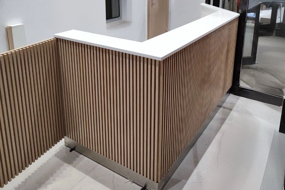 Стойка ресепшен из акрилового камня с белой столешницей и деревянными рейками, современный интерьер